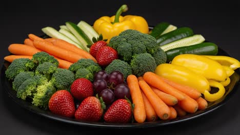 a vibrant array of fresh vegetables and juicy fruits artfully arranged on a black plate, showcasing a variety of colors and textures for a healthy lifestyle.
