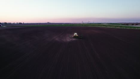 Vista-Aérea-Detrás-Del-Tractor-Arando-Un-Campo-Al-Atardecer