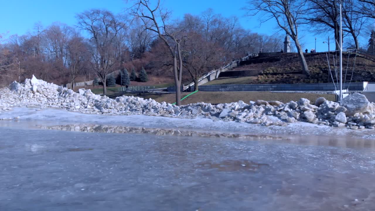 tomada panorámica de un parque en el borde de un río congelado con montones de fragmentos de hielo y escombros en el borde del río