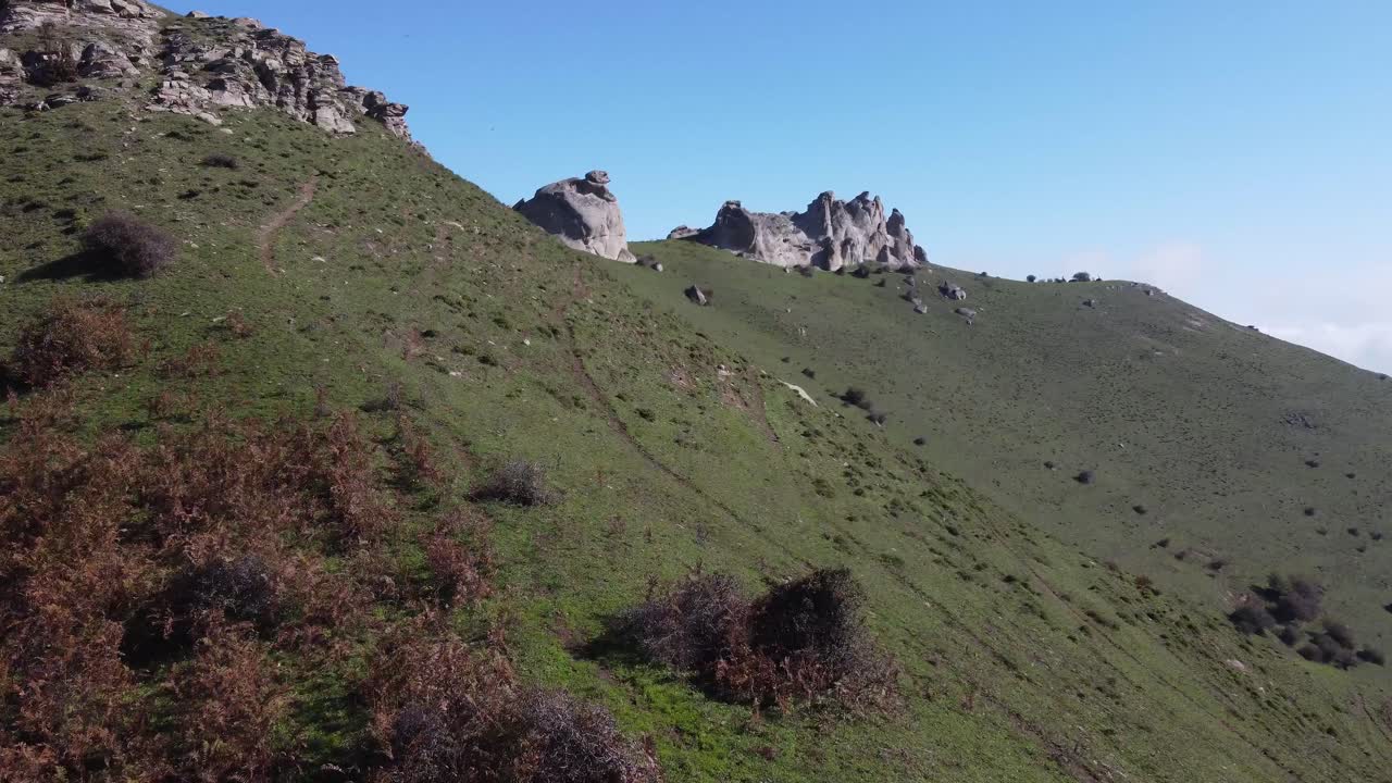 Volo a bassa quota lungo un pendio erboso su per la montagna verso affioramenti di roccia granitica