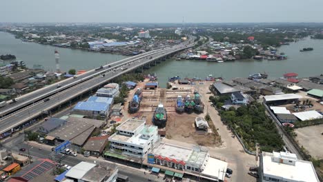 aerial view of a bustling shipyard with boats undergoing maintenance near a bridge spanning a river
