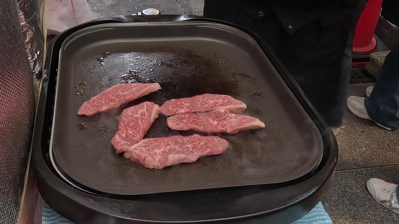 立ち上る湯気と共に、熱い石のグリルで焼ける霜降りの上質な牛肉の薄切りのクローズアップ。