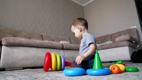 boy in grey t-shirt plays with pyramid on the floor. child breaks the pyramid. low angle view.