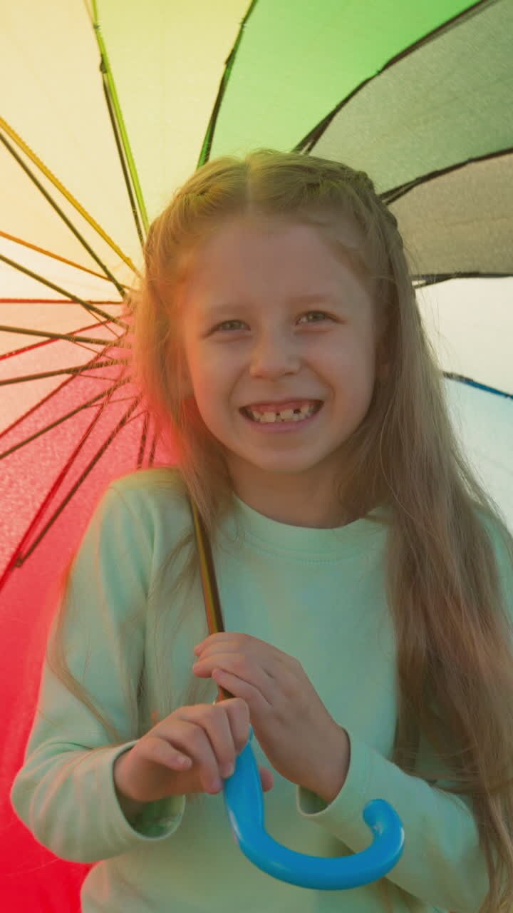 Kid moves motley parasol along riverbank. Child umbrella captures sun rays creating mosaic of hues dancing upon dampened earth. Whimsical display