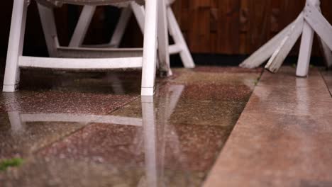 vista en cámara lenta de gotas de lluvia cayendo afuera en el pavimento con silla blanca