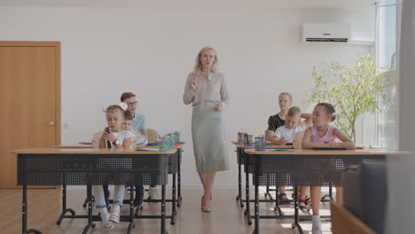 a young school teacher walks around the classroom and tells the children the topic of a new lesson