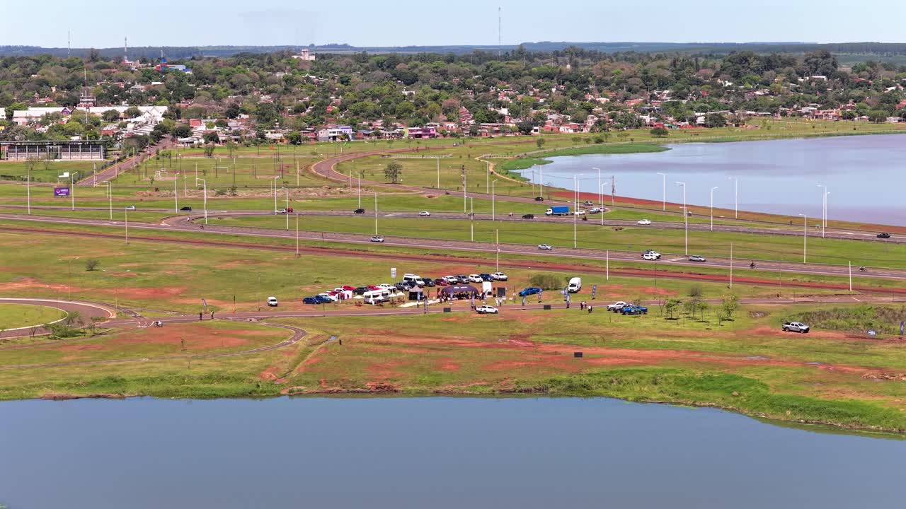 A wide aerial shot of Posadas, Misiones, showing the coastal road (Acceso Sur), new development, and a temporary outdoor market or event space by the water