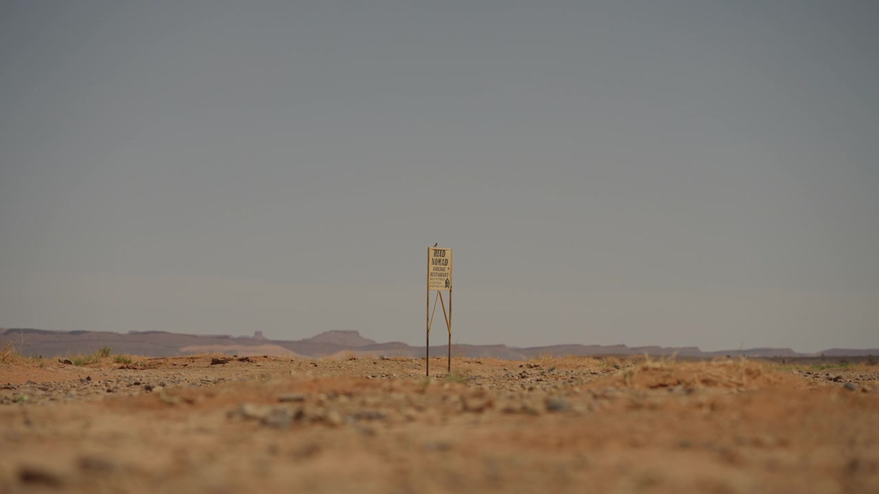Small lone yellow warning sign standing alone in vast rocky Sahara desert plain under hazy sky in southern Morocco