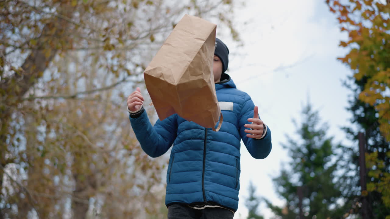 niño caminando a lo largo de los árboles secos pensativo, da la vuelta su bolsa al revés vertiendo hojas secas en el suelo. vibrante paisaje de otoño en el fondo con follaje colorido y una valla rústica