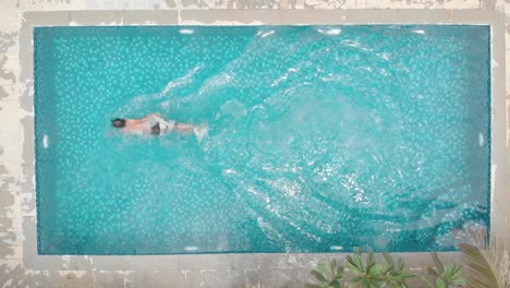 overhead shot of young fit man loose casual swimming trunks freestyle stroke front crawl small private home pool