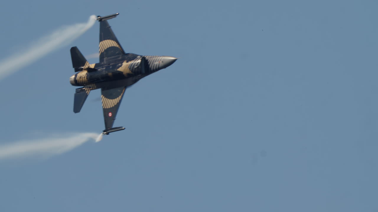 Svart och guld stridsflygplan med rökspår på blå himmel