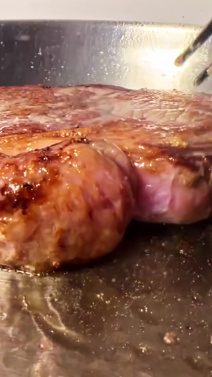Un primo piano di una bistecca che sfrigola su una piastra calda, mostrando la sua consistenza succosa e la superficie che si sta dorando. Ideale per contenuti culinari o tutorial di cucina