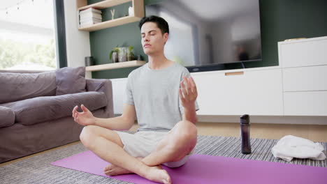 biracial man practicing yoga meditation and breathing sitting on floor, copy space, slow motion