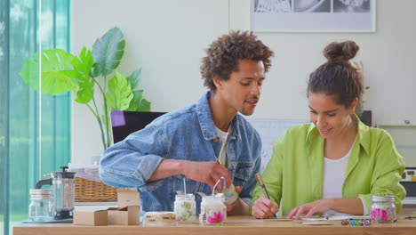 Pareja-Que-Dirige-Negocios-En-Línea-Desde-Casa-Haciendo-Velas-Boutique-Escribiendo-Etiquetas-Para-Productos