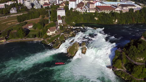 cámara lenta: tiro de seguimiento de un barco turístico rojo que lucha contra la cascada rugiente rheinfall en schaffhausen en suiza