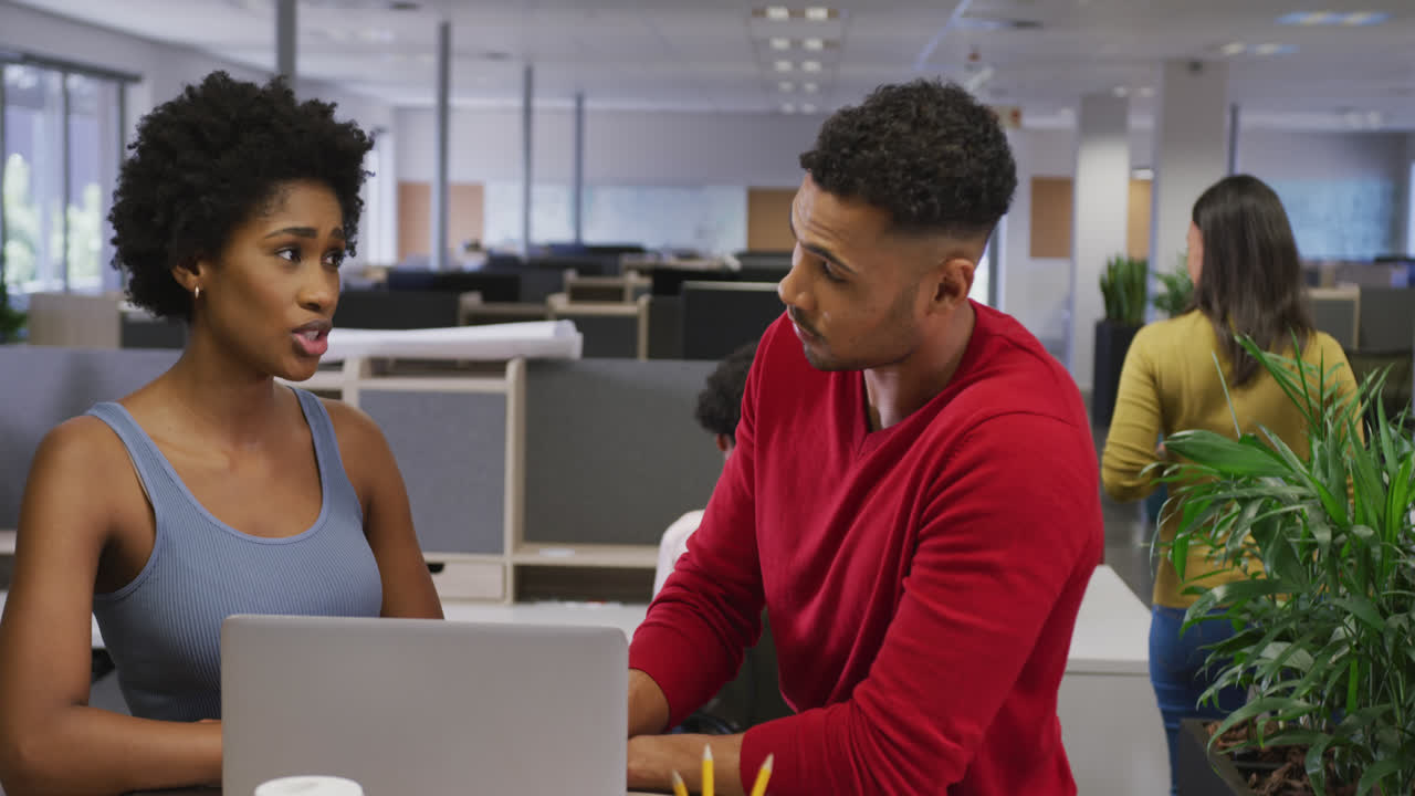 Diverse male and female business colleagues talking and using laptop in office
