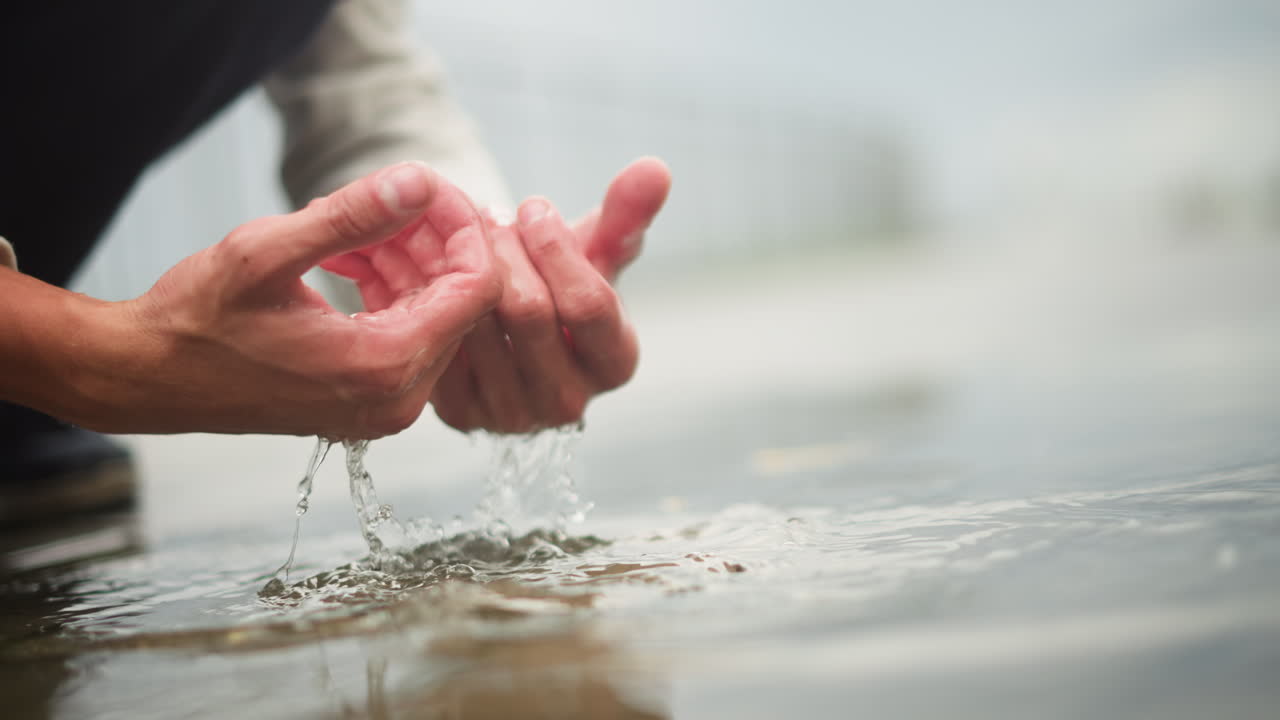 백인 손이 빗물을 받아 튀는 모습, 오목하게 모은 손바닥에서 물방울이 흩날리고, 젖은 신발이 보이며, 흐릿한 다리 배경, 활기찬 도시의 가랑비, 즐거운 촉각의 순간, 활기찬 움직임