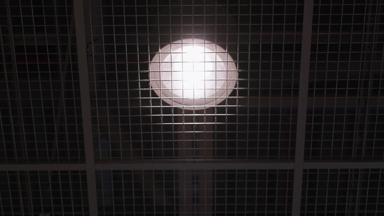 Detalhe do teto de aeroporto com uma lâmpada suspensa brilhante atrás de uma grade de metal, criando um padrão geométrico limpo no interior de um terminal moderno