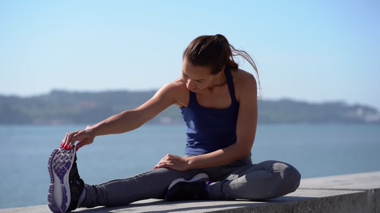 Focused sporty girl stretching leg at riverside