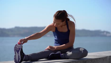 Konzentriertes-Sportliches-Mädchen,-Das-Am-Flussufer-Sein-Bein-Streckt