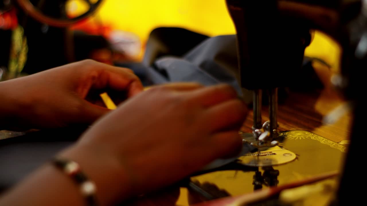 Woman in Africa using antique sewing machine to sew black fabric