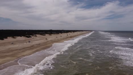 drone volando sobre las olas del océano con autos conduciendo en la playa de arena, mar de las pampas en argentina