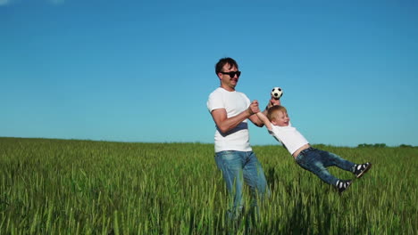 familia feliz: padre dando vueltas a su hijo con camiseta blanca y vaqueros