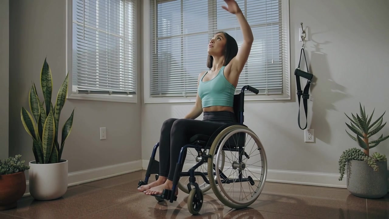 Sitting upright, woman looking up lifting right arm in corner, touching wheelchair