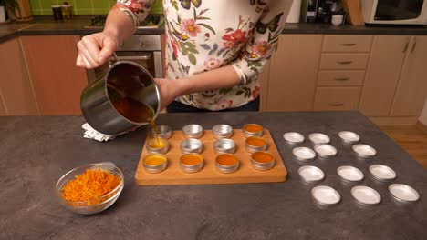 zoom lento en la toma de primer plano de una mujer joven que vierte un bálsamo de cera de abeja líquido amarillo-naranja caliente en recipientes de aluminio circulares vacíos