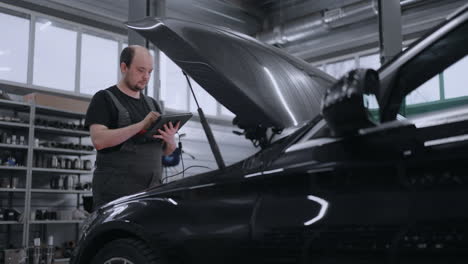 male mechanic uses a tablet computer with an augmented reality diagnostics software. specialist inspecting the car in order to find broken components inside the engine bay. modern car service.