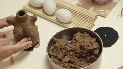 hands sculpting and refining the details of a female body shape made of recycled egg carton air dry clay