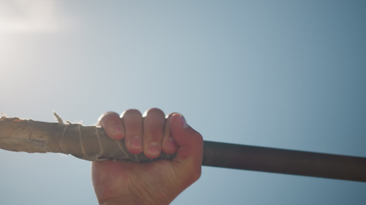 Luz intensa en exteriores, silueta de una mano sujetando una barra, escena de alto contraste con luz solar y pose atlética, inspiradora imagen de entrenamiento en exteriores con una mano agarrando una barra con el cielo iluminado por el sol de fondo