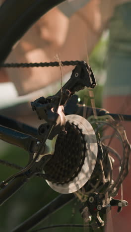 close-up of lady bending to rotate bike pedal with her hand, causing back tire to spin, capturing mechanics and motion of cycling against green foliage backdrop