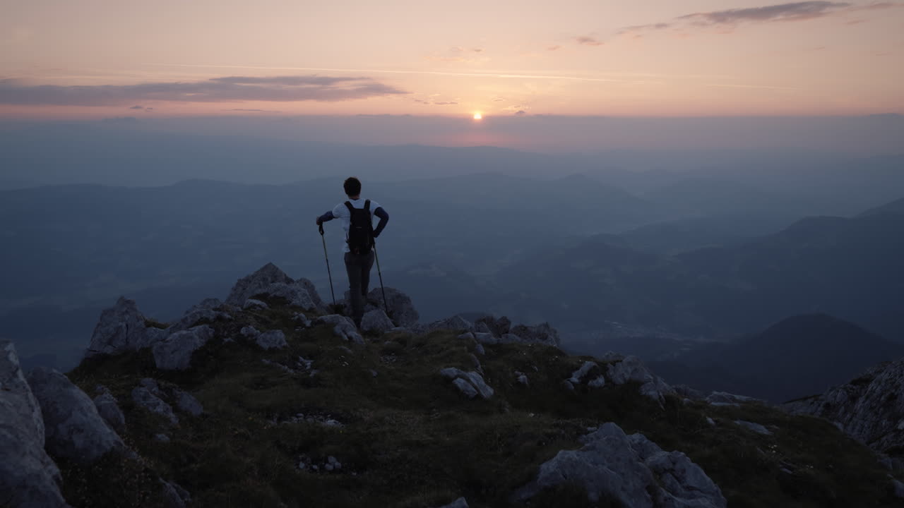 cámara siguiendo a un joven excursionista que ha llegado al borde de una montaña para admirar un hermoso amanecer