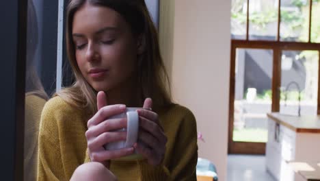 mujer con taza de café mirando por la ventana en casa