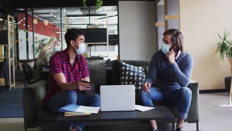 personas de negocios diversas usando máscaras usando computadora portátil y pasando por el papeleo en la oficina moderna