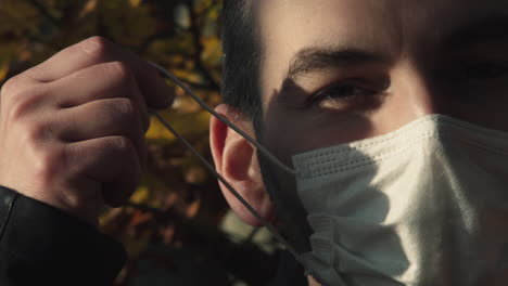 taking off face mask outside, caucasian man head closeup, copy space and forest in background, end of covid pandemic