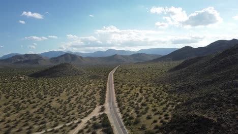 una toma aérea de una carretera solitaria en el desierto del sudoeste de estados unidos con arbustos verdes y un paisaje árido en una meseta con montañas en el horizonte