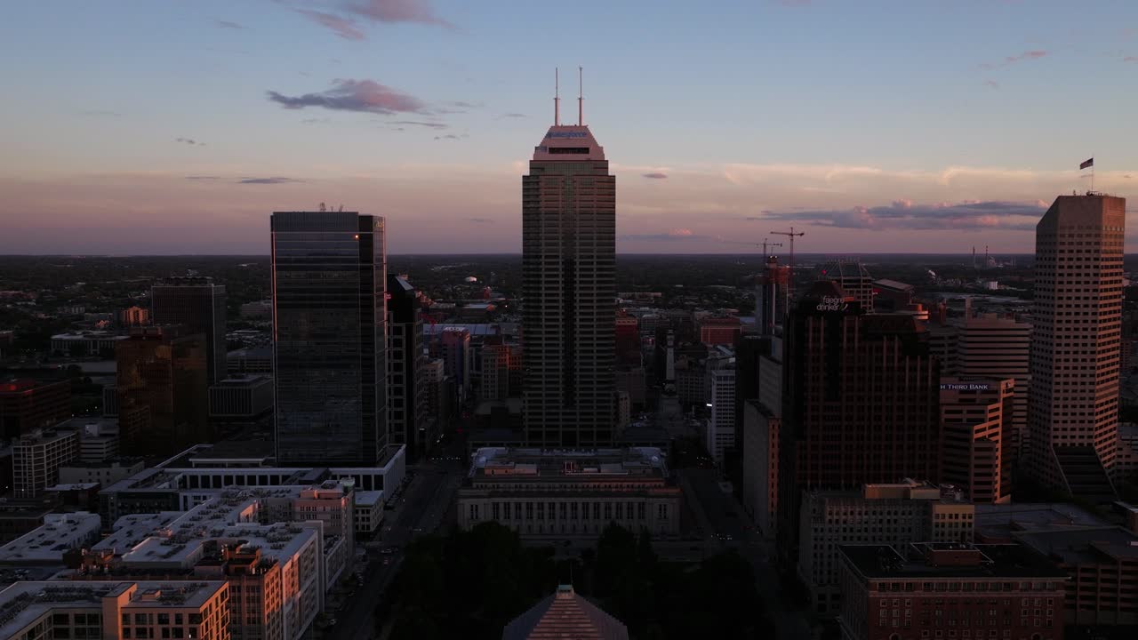Ripresa aerea in allontanamento dello skyline del centro di Indianapolis al tramonto in una giornata estiva. Grattacieli e punti di riferimento della città nella calda luce della sera