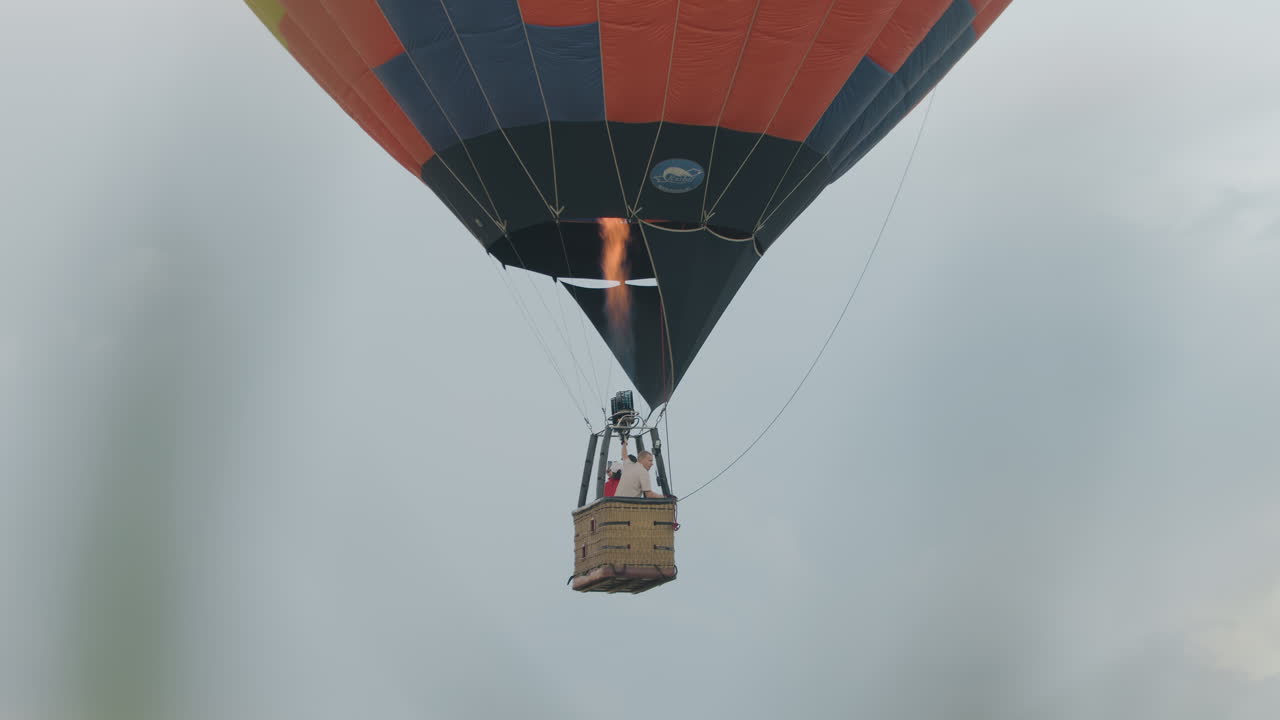 Three people float midair inside hot air balloon as man in white top increases flame using control mechanism while others observe scenery