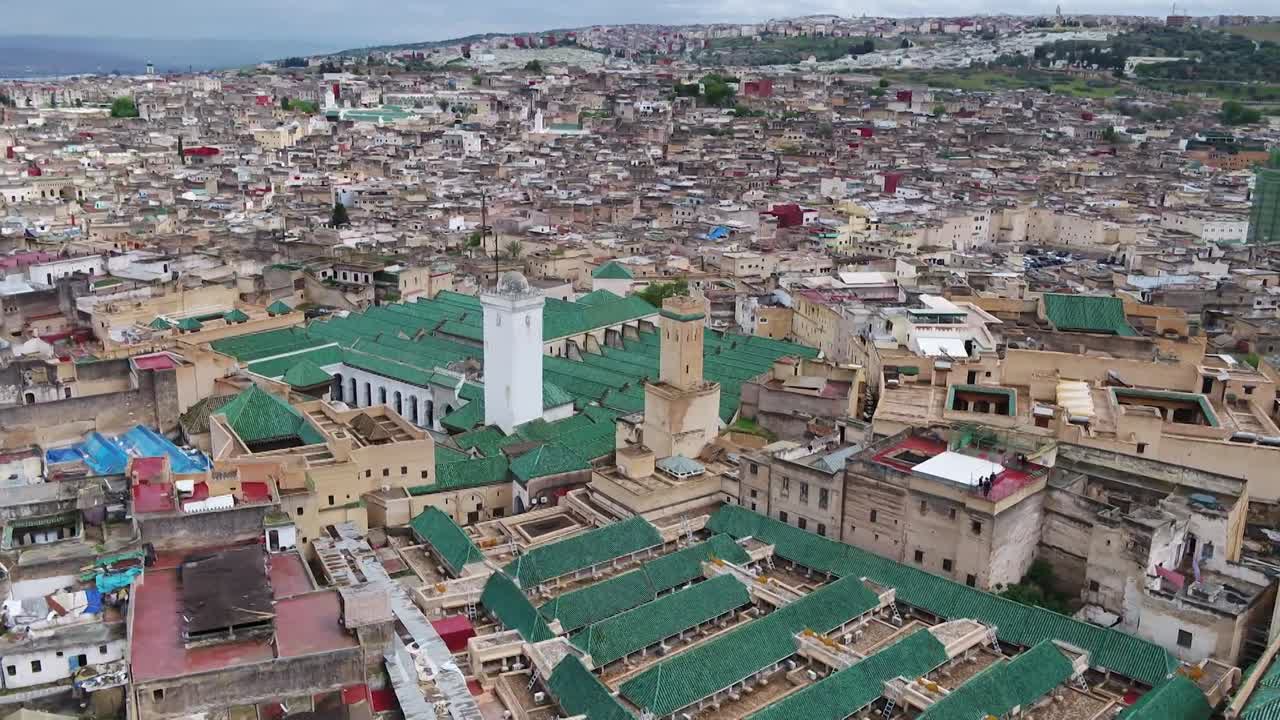 Ampia ripresa aerea con drone della storica area della moschea Al-Qarawiyyin a Fez. Presenta gli ampi tetti di tegole verdi, molteplici antichi minareti e il denso paesaggio urbano tradizionale della vecchia medina.
