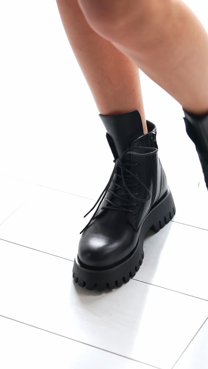 Model showing the elegant black leather low boots with tractor soles. Fashionable footwear show at white floor backdrop. Top view. Vertical video