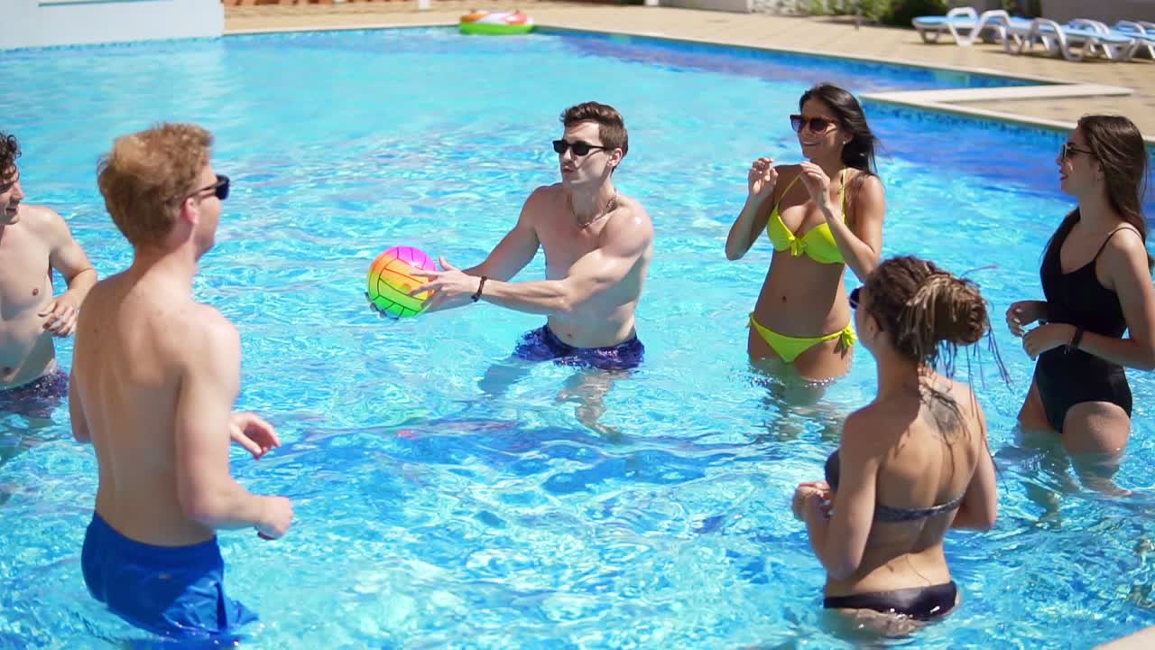 Group of young friends playing volleyball in the swimming pool. Summertime pool party. Slow Motion shot