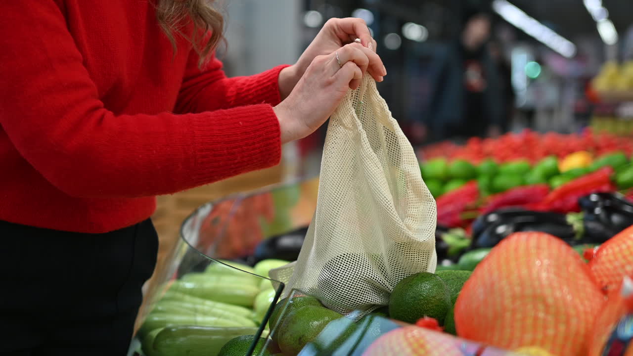 Woman picking avocados in a reusable bag in a store. Ecology and Earth Day thematics. Slow motion