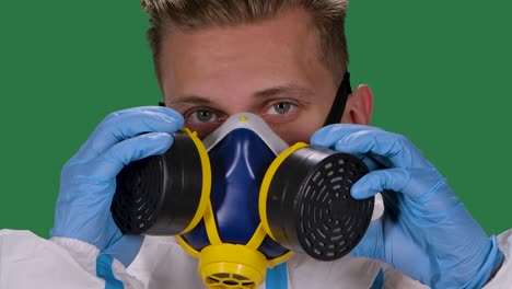 retrato de un virólogo masculino en un traje de protección blanco y guantes quirúrgicos pone y luego quita el respirador médico. pantalla verde, llave de croma. cámara lenta. primer plano