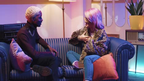 african american man and caucasian stylish woman in sunglasses talking while sitting on couch in a retro party at home