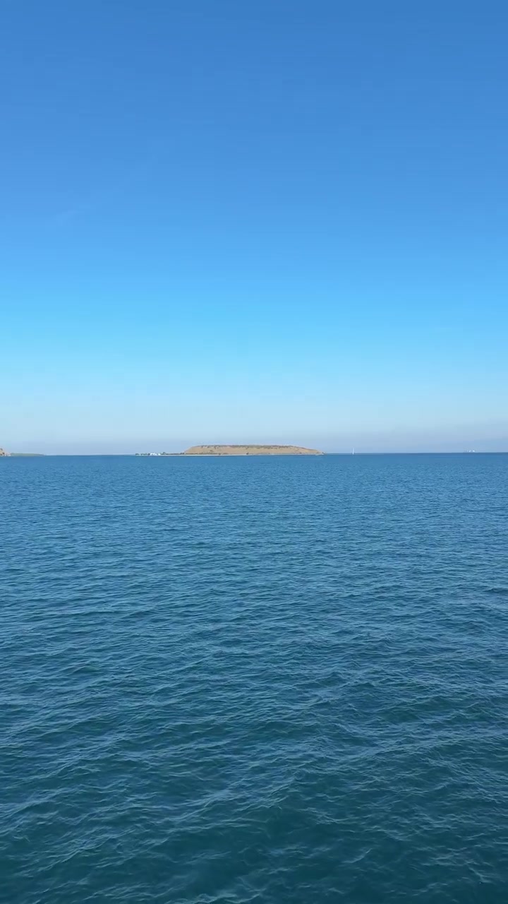 Roligt blåt havvand med fjern ø og klar himmel