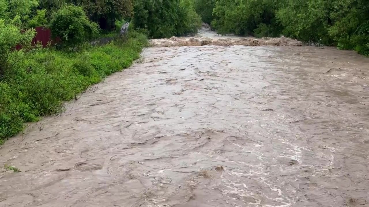 Overflowing Tarnava Mica River after heavy rain in Romania. Muddy, brown water flowing rapidly, creating a dangerous and destructive flood