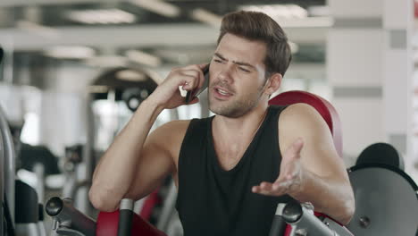 Hombre-Atleta-Hablando-Con-Teléfono-Inteligente-Después-De-Entrenar-En-Una-Máquina-Deportiva-En-El-Gimnasio