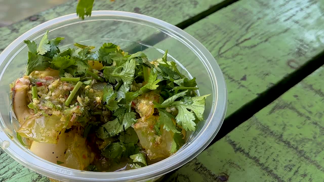 Close-up of a squid dish garnished with fresh herbs in a clear bowl on a green table.
